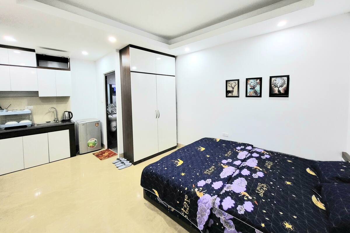 A compact hotel room with a bed, kitchenette, and a small bathroom.