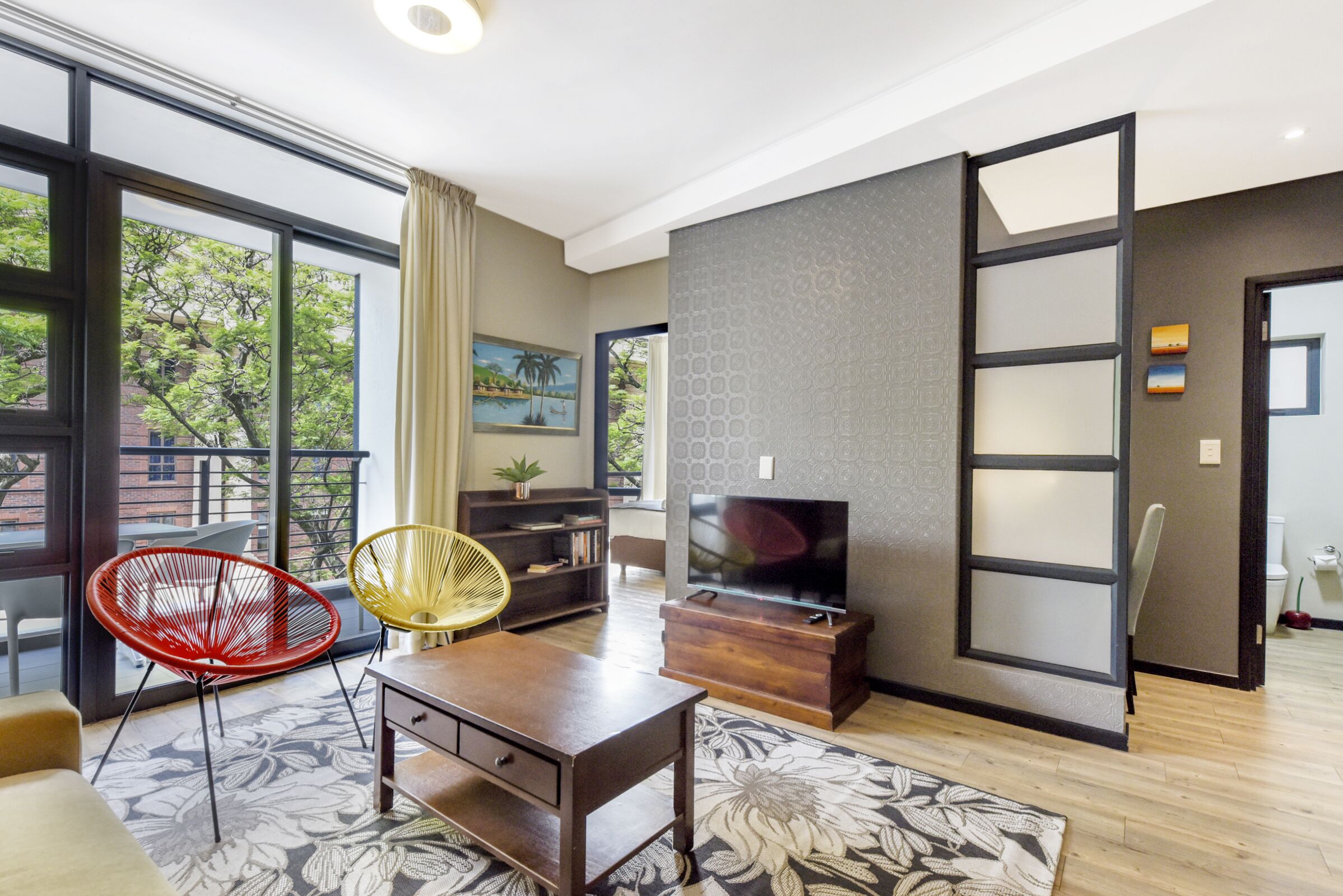 A modern living room with a large window, a TV, a sofa, and a red chair.