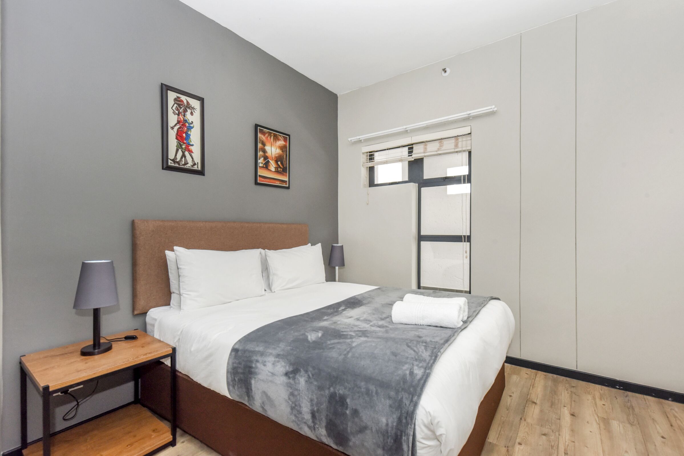 A modern hotel room with a large bed, a nightstand with a lamp, and two framed pictures on the wall.