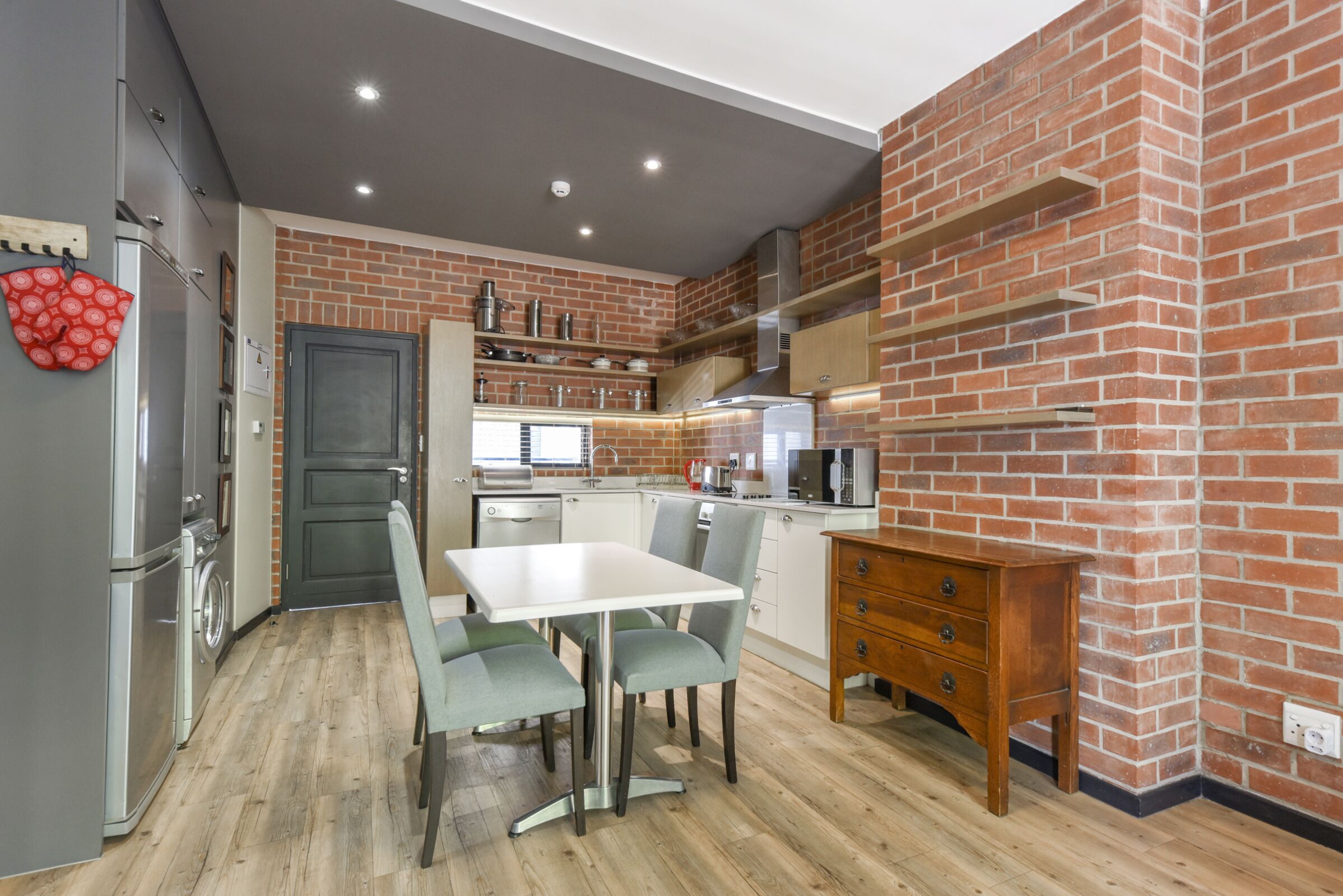 Una cocina moderna con pared de ladrillo, electrodomésticos de acero inoxidable y un comedor con mesa y sillas.