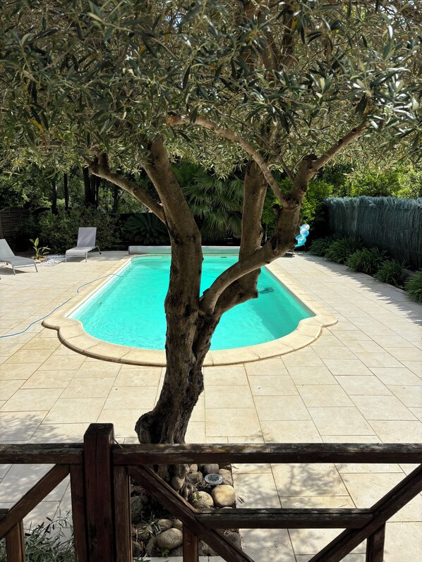A swimming pool surrounded by a tiled patio, a wooden fence, and a tree. - Magnifiquement calme, villa spacieuse de 4 chambres avec piscine privée (Sorède)
