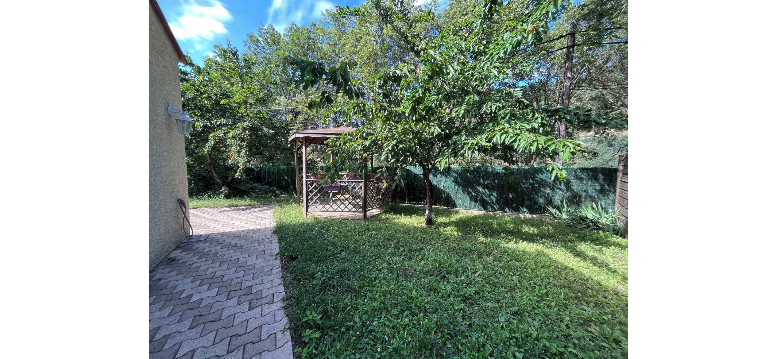 A paved pathway leading to a gazebo in a garden with a fence and trees.