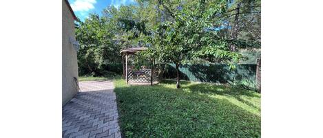 A paved pathway leading to a gazebo in a garden with a fence and trees.