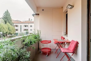 A balcony with a table and chairs, a red table lamp, and a view of buildings and trees. - pieno centro storico a poche centinaia di metri dal mare, appartamento di 95 mq (Pesaro)