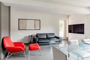 A modern living room with a black leather sofa, a red armchair, a glass coffee table, and a flat-screen TV mounted on the wall. - pieno centro storico a poche centinaia di metri dal mare, appartamento di 95 mq (Pesaro)