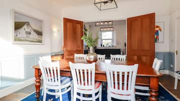 A dining room with a wooden table and white chairs, a vase with flowers, and a painting on the wall.