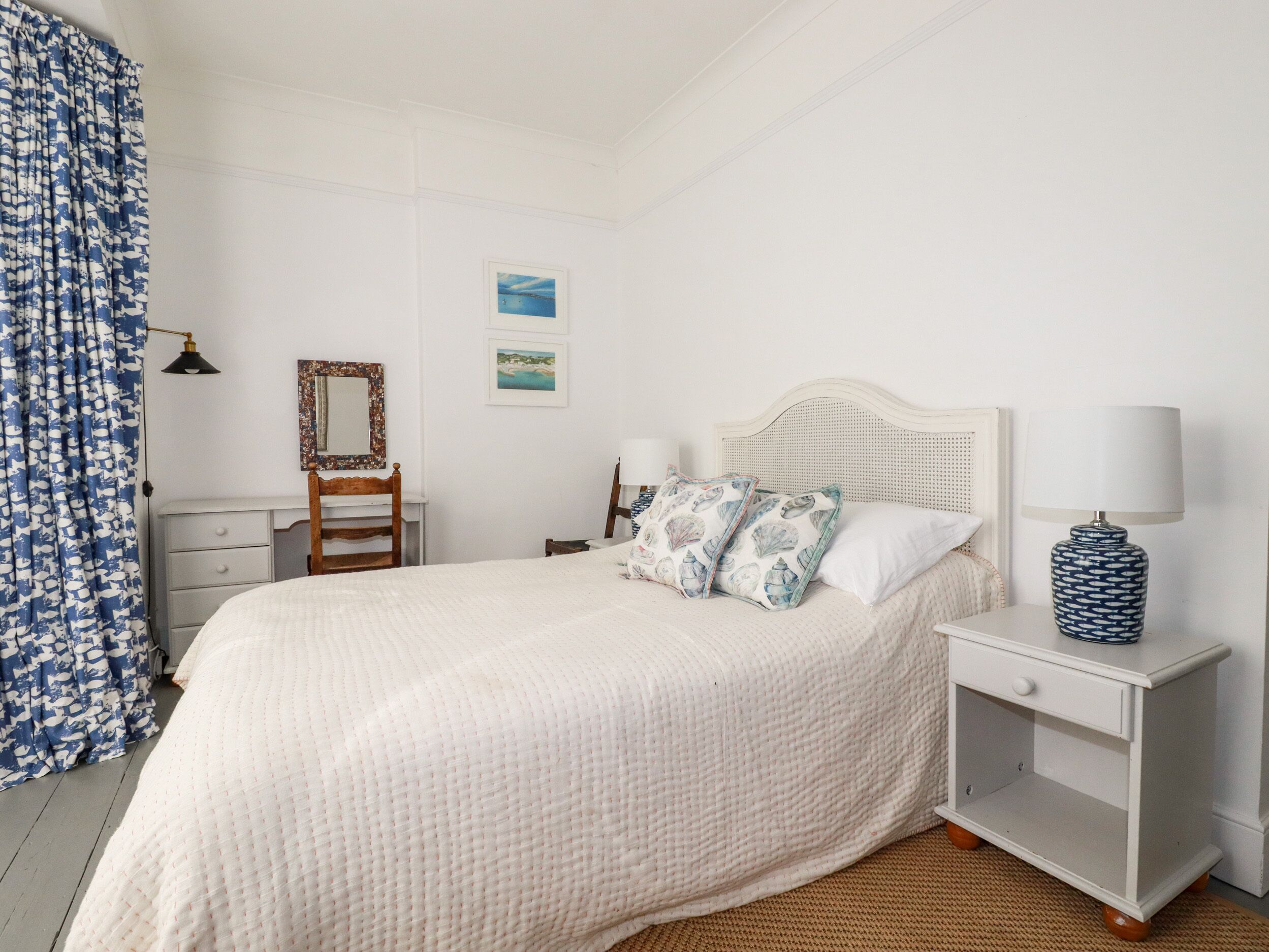 A bedroom with a bed, bedside table, lamp, dresser, and a mirror.