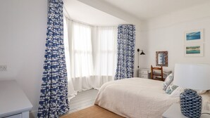 Um quarto com uma cama, uma escrivaninha, uma cadeira, um abajur e um vaso.