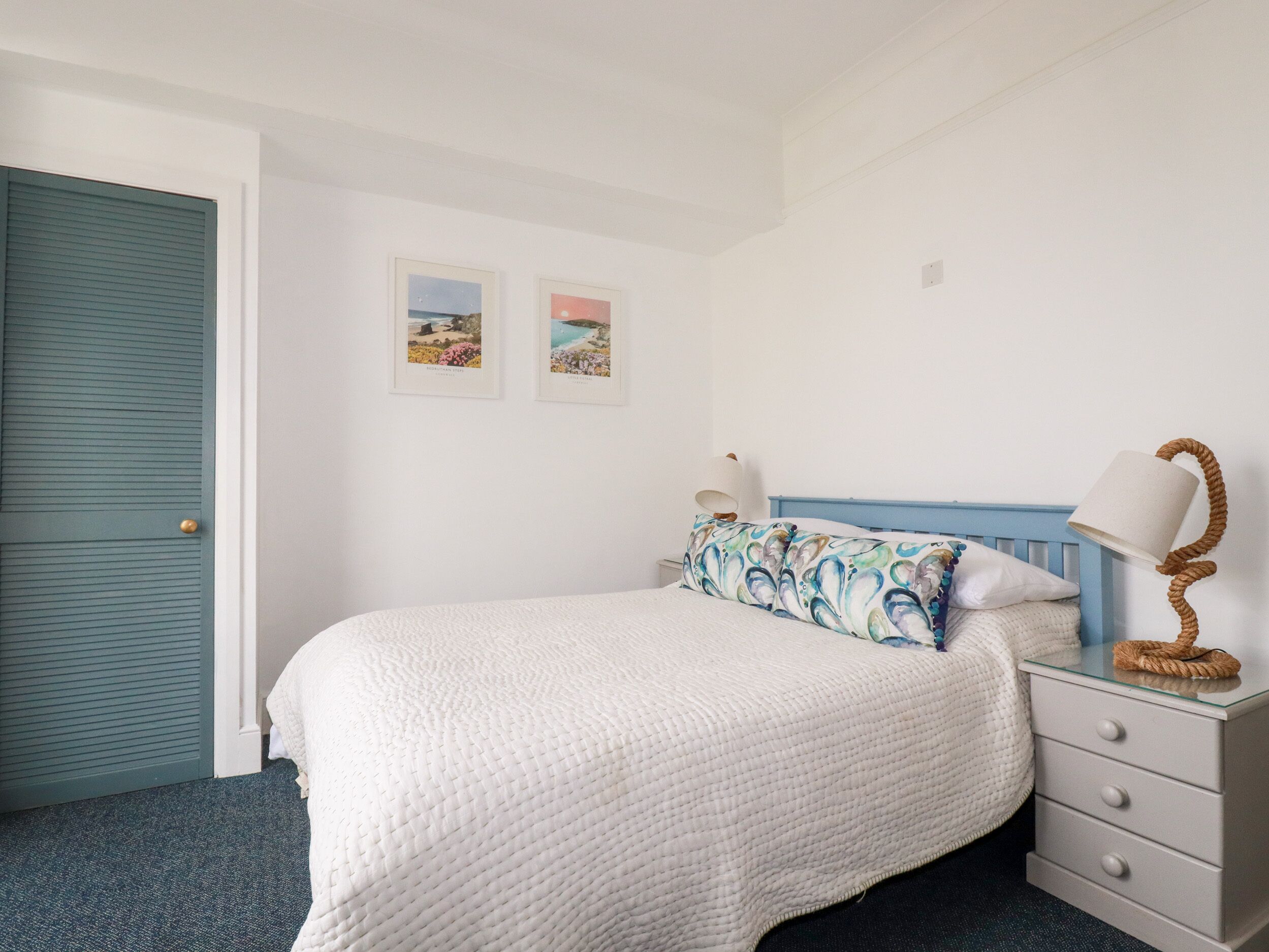 A bedroom with a bed, a nightstand, a lamp, and two framed pictures on the wall.
