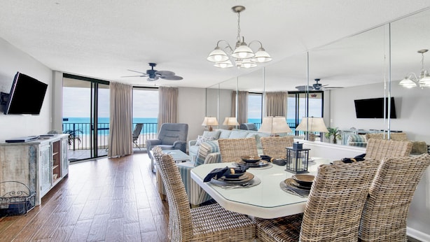 A spacious living area with a balcony overlooking the sea, furnished with wicker chairs and a dining table.