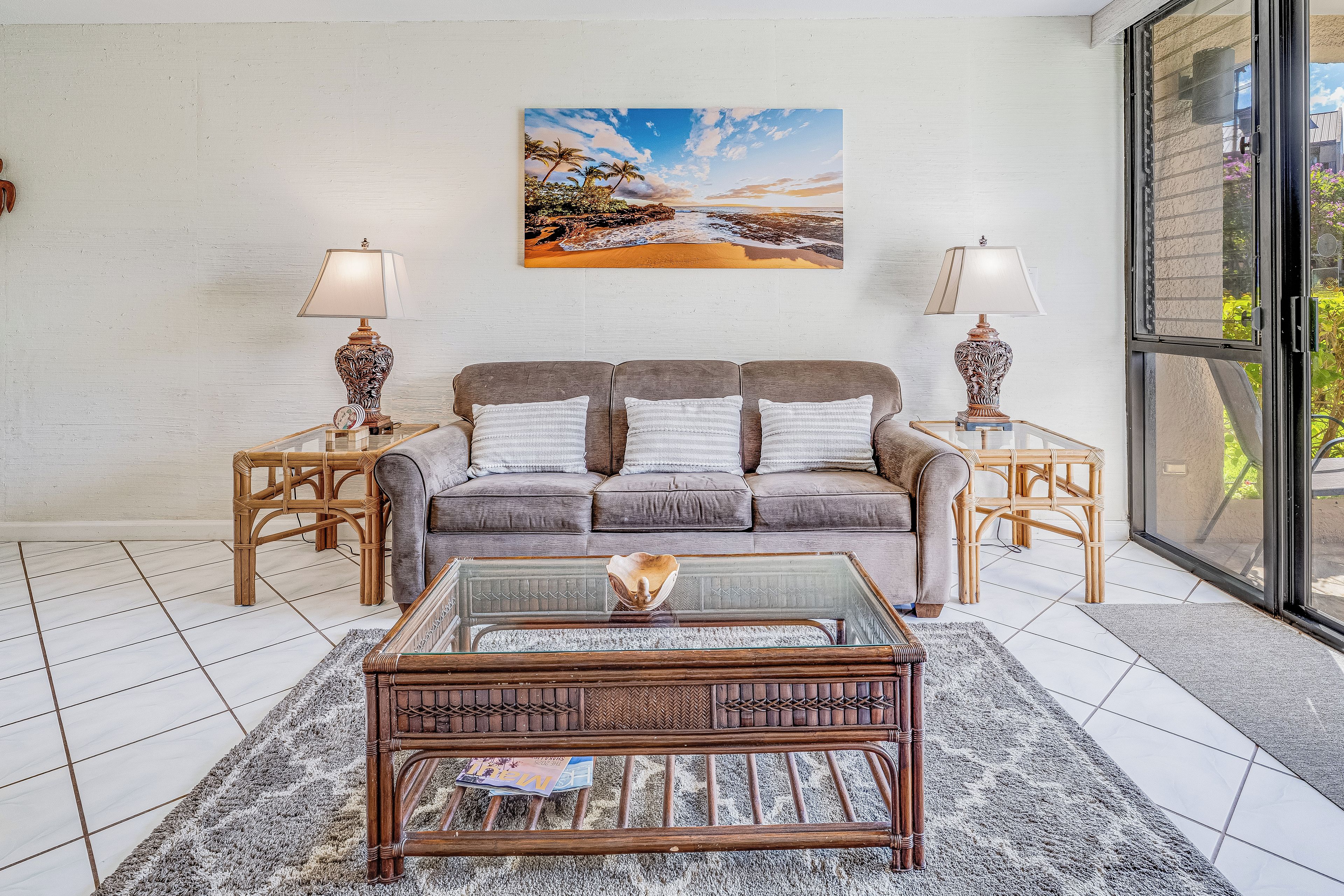 A living room with a sofa, two side tables with lamps, a coffee table, and a large beach painting on the wall.