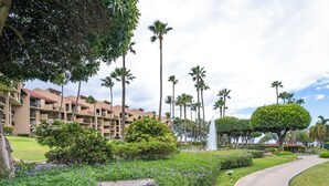Un hotel con un jardín ajardinado, palmeras y una fuente.