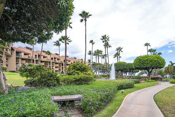 Een hotel met een aangelegde tuin, palmbomen en een fontein.