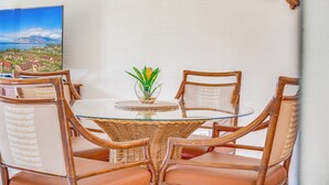 Una mesa de vidrio redonda con sillas de mimbre, una planta pequeña en maceta y un cuadro con un paisaje costero.