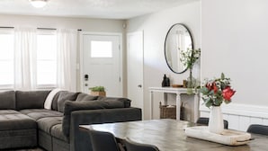 A modern living room with a sectional sofa, a dining table, and a fireplace. - Walk to Groceries—Sleeps 8—Game Room + Patio + Parking for 4 (Lubbock)