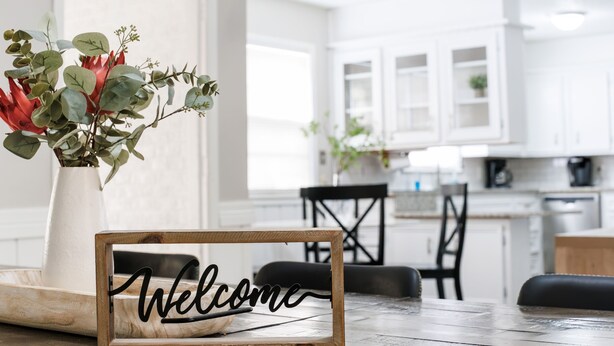 A wooden table with a 'Welcome' sign and a vase of flowers in a white pot. - Walk to Groceries—Sleeps 8—Game Room + Patio + Parking for 4 (Lubbock)