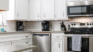 A modern kitchen with white cabinets, a stainless steel dishwasher, a coffee maker, and a microwave. - Walk to Groceries—Sleeps 8—Game Room + Patio + Parking for 4 (Lubbock)