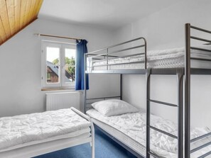 Cozy dormitory room with a bunk bed and single bed, featuring a window with an outside view and a radiator.