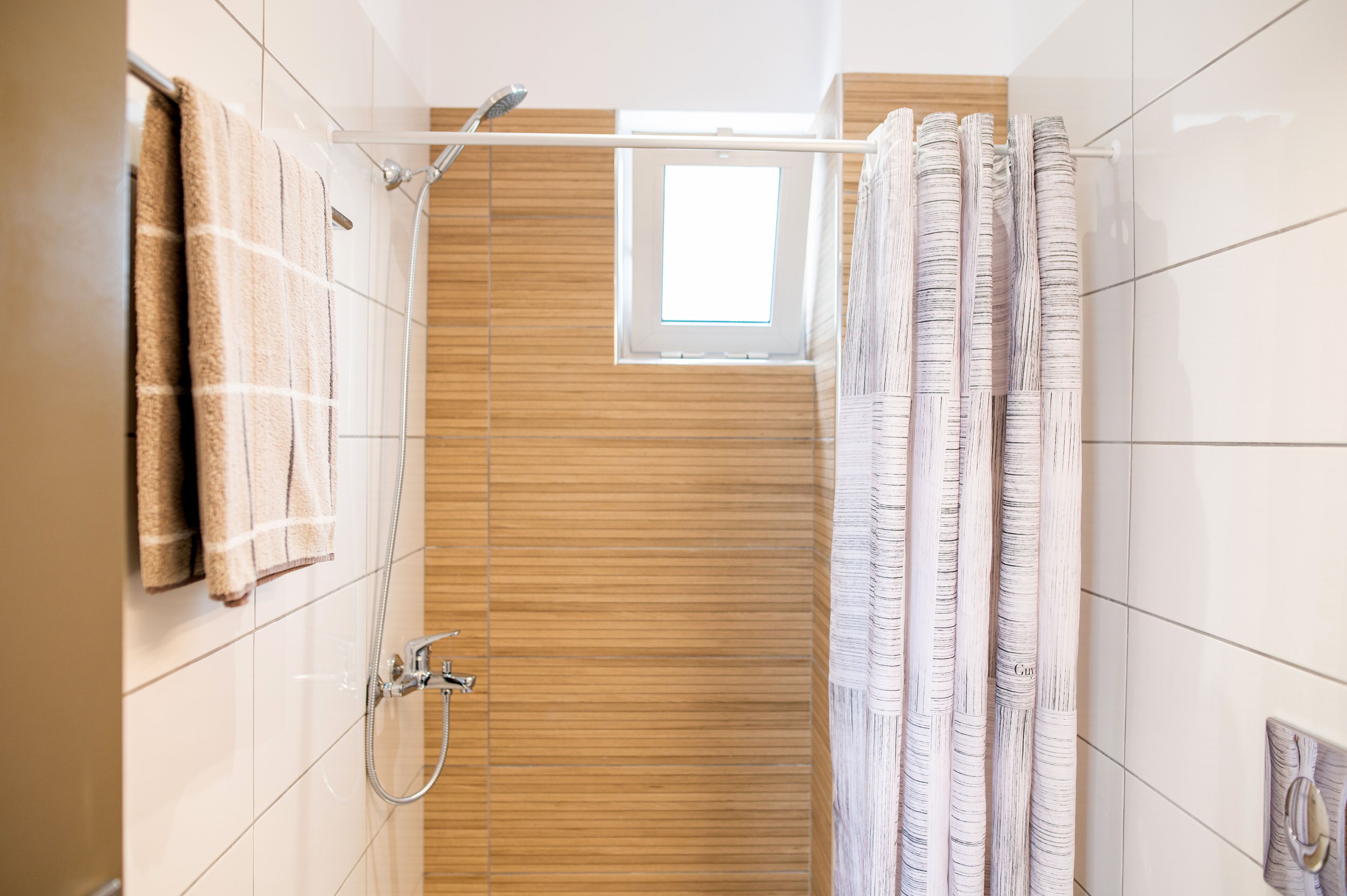 A modern bathroom with a shower, wooden paneling, and a window.