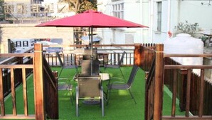A patio area with a grill, chairs, and a red umbrella.
