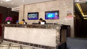 A hotel reception area with a marble counter, two monitors on the wall, and a sign indicating no smoking.