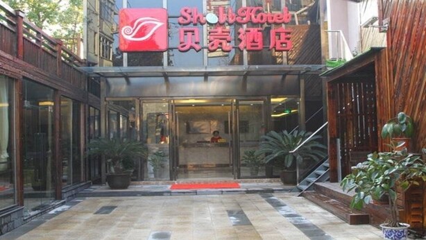 A hotel entrance with a reception desk, potted plants, and a staircase leading to the entrance.