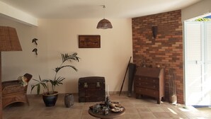 Uma sala de estar acolhedora com parede de tijolos, um baú de madeira, uma cadeira de vime e uma planta em vaso.