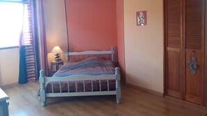 Quarto com cama, ventoinha no teto, guarda-roupa de madeira e janela com cortinas.