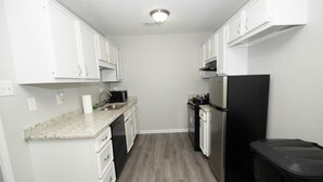 Cocina compacta con armarios blancos, un refrigerador de acero inoxidable, microondas y lavavajillas.
