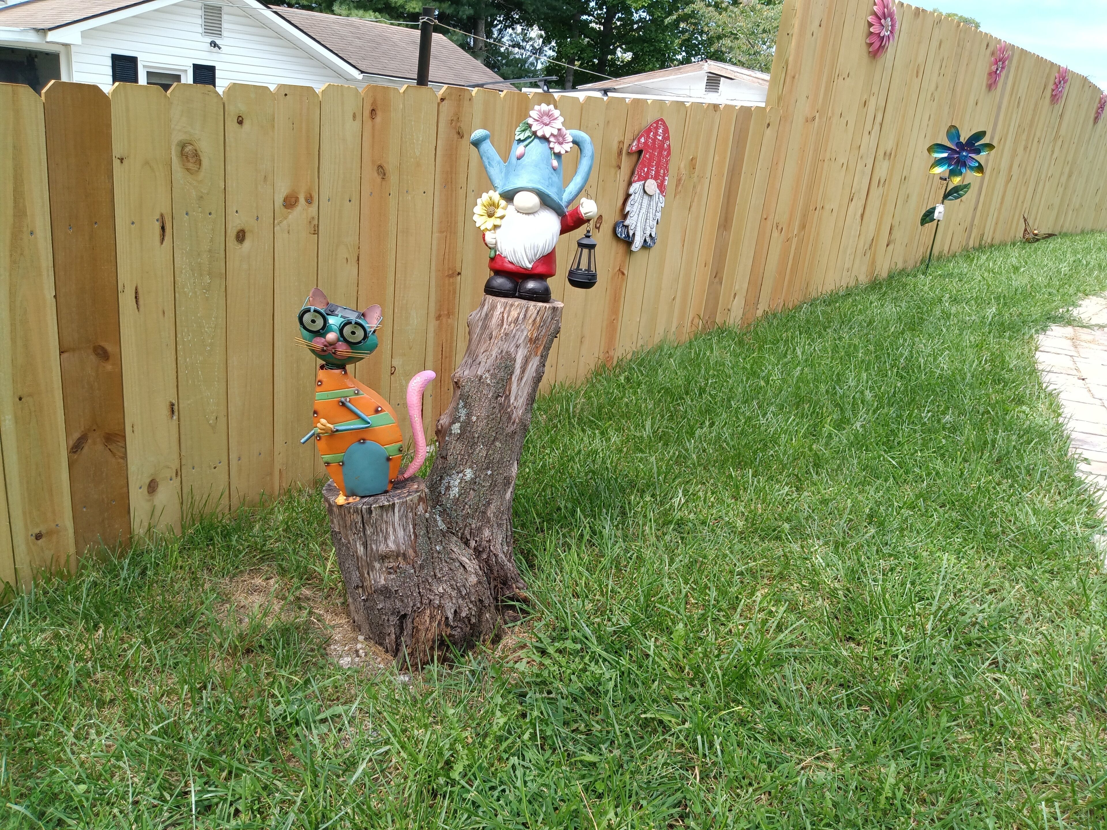 Une clôture en bois ornée de figurines de gnomes décoratifs et d’une souche d’arbre.