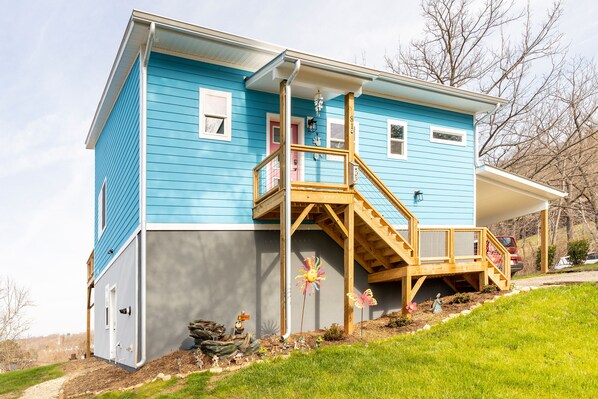 Une maison à deux  étages, avec une façade bleue, un escalier en bois et un petit porche.
