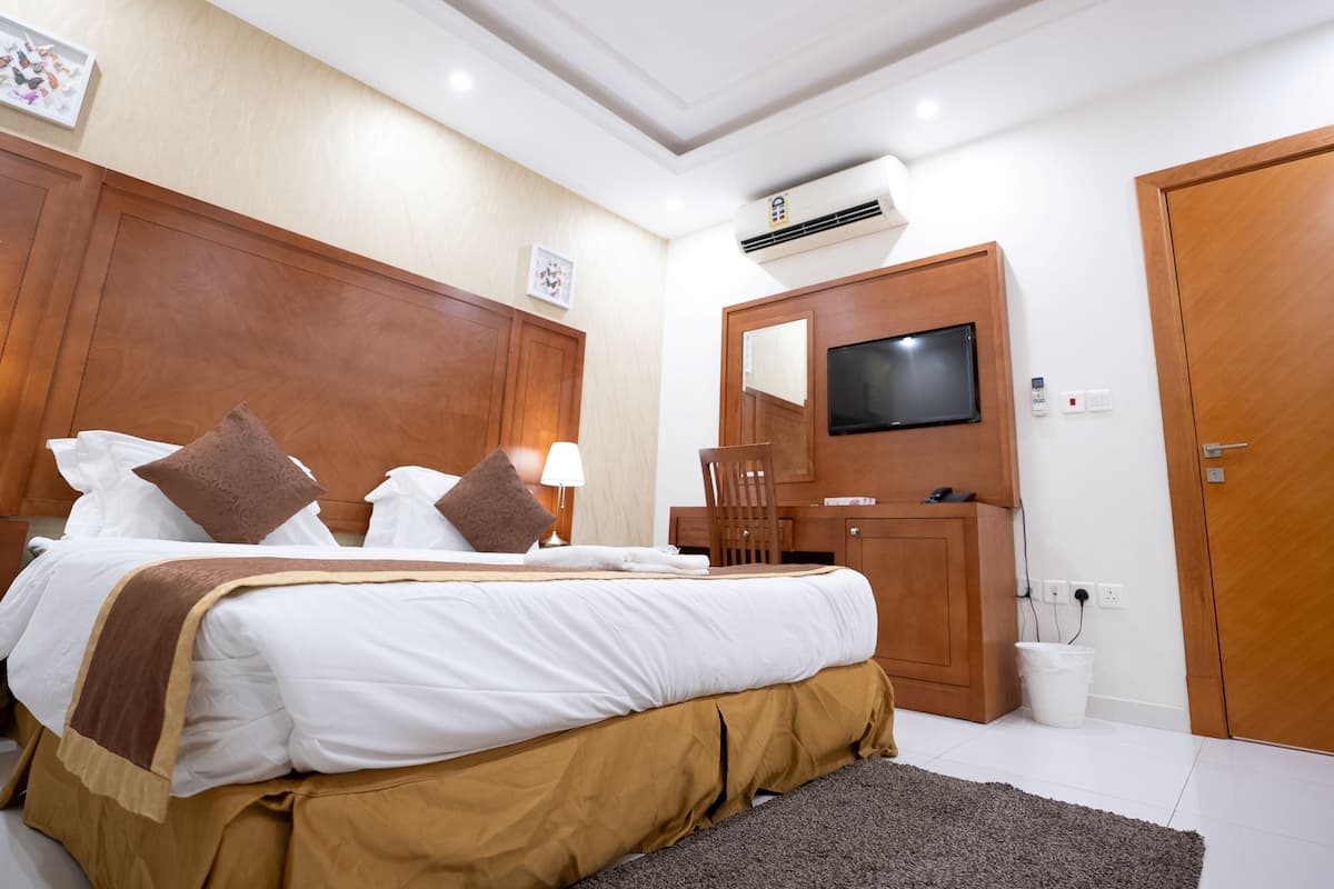 A hotel room with a large bed, a wooden headboard, a TV mounted on the wall, and a desk with a chair.