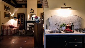 Un salon chaleureux avec un canapé et une petite table, une cuisine dotée d’un plan de travail en marbre et d’une cuisinière à gaz, et une arche en briques reliant les deux espaces.