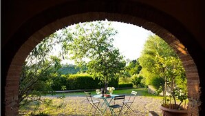 Un espace extérieur aménagé en patio, avec une arche en briques, une table entourée de chaises et des plantes en pot.