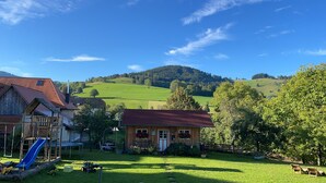 Une maison de campagne avec un toit rouge, une structure de jeu en bois et une pelouse.