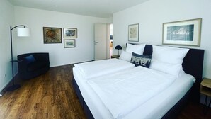 Une chambre d’hôtel moderne, dotée d’un grand lit, d’une chaise, d’un bureau et d’œuvres d’art accrochées aux murs.