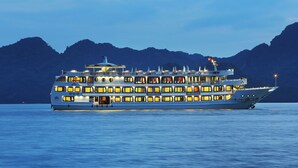 A multi-deck cruise ship with several levels of windows and balconies, set against a mountainous backdrop. - Bigfun Cruises (Tuan Chau)