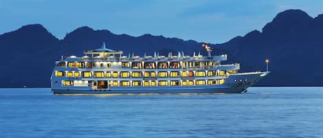 Un crucero de múltiples cubiertas con varios niveles de ventanas y balcones, con montañas al fondo.