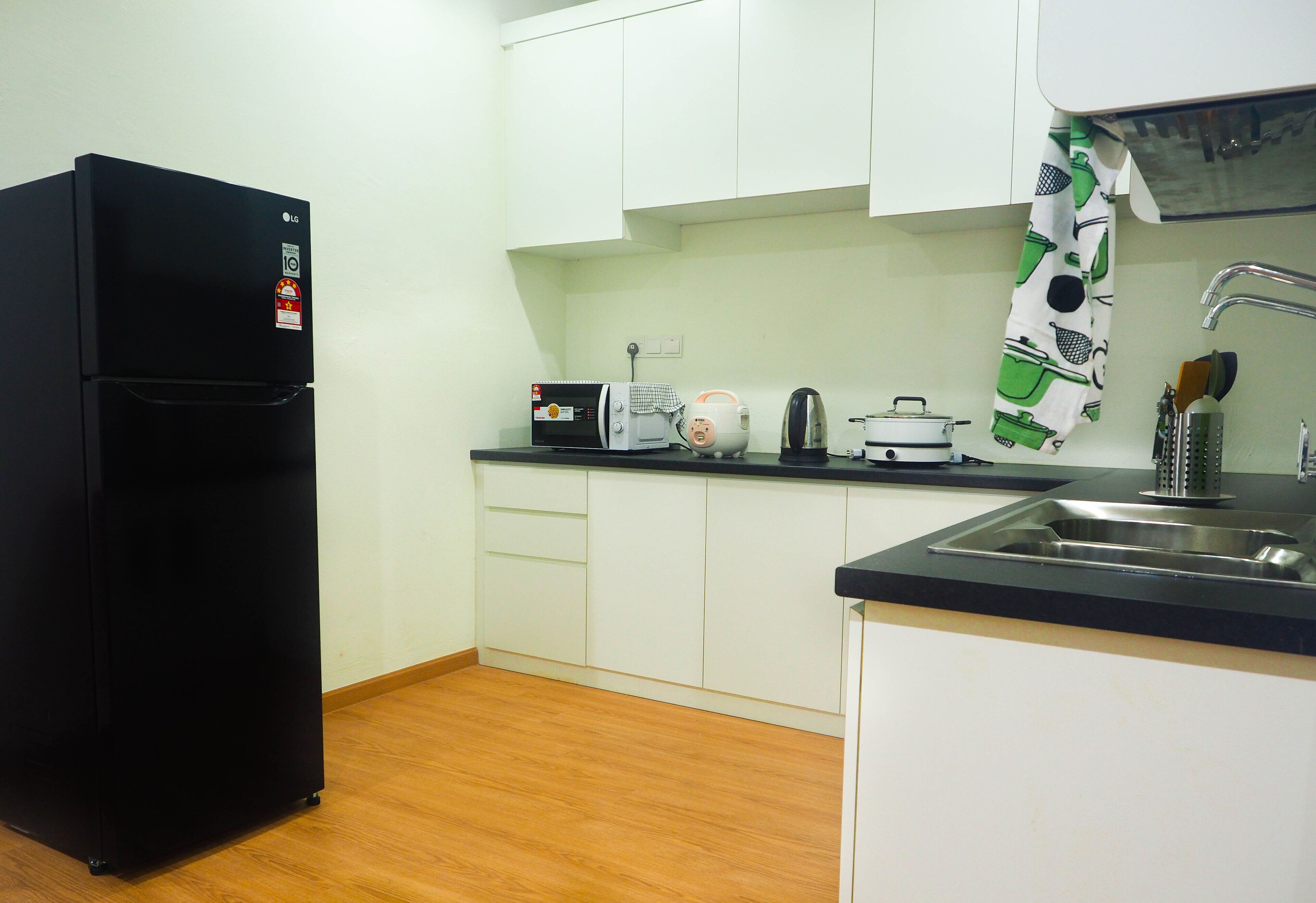 A compact kitchen with white cabinets, a black refrigerator, a coffee maker, and a kettle.