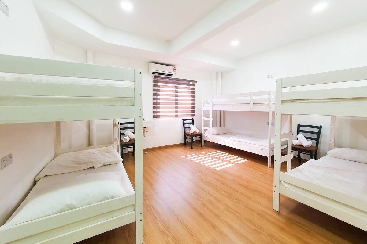 Ein Zimmer mit Etagenbetten, Holzboden, einem Fenster mit Jalousien und einem Stuhl.