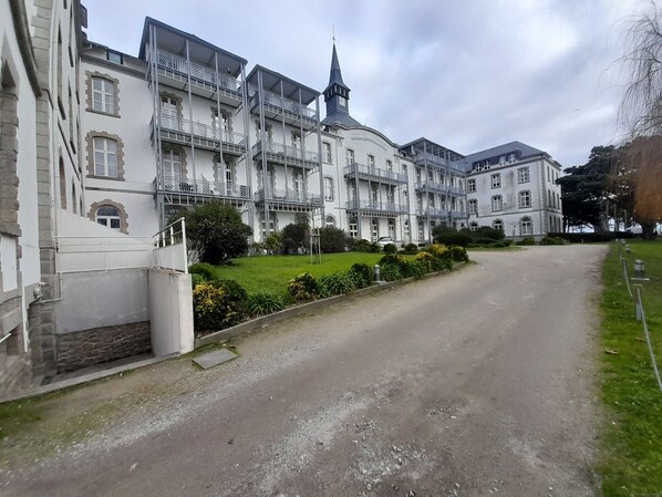 Un grand bâtiment à étages, doté d’une tour imposante, qui ressemble probablement à une église, et d’une pelouse bien entretenue avec une allée gravillonnée.