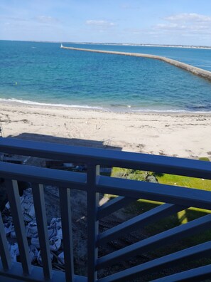 Une vue sur la plage avec une rambarde en bois, un ciel dégagé et une mer calme.