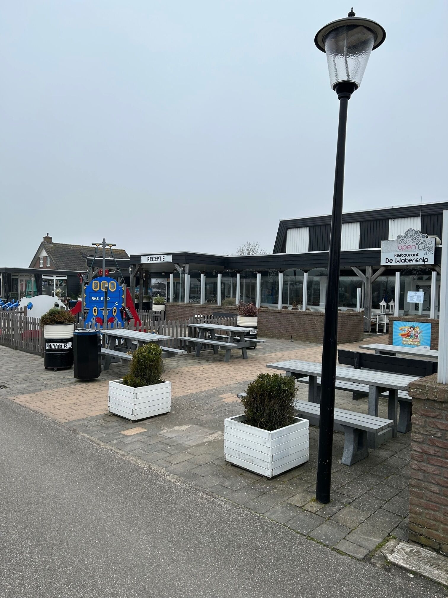 A waterfront restaurant with outdoor seating, a reception area, and a play area for children.