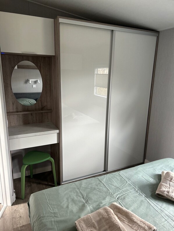 Un dormitorio con cama, un taburete verde, un espejo, un armario y una ventana pequeña.