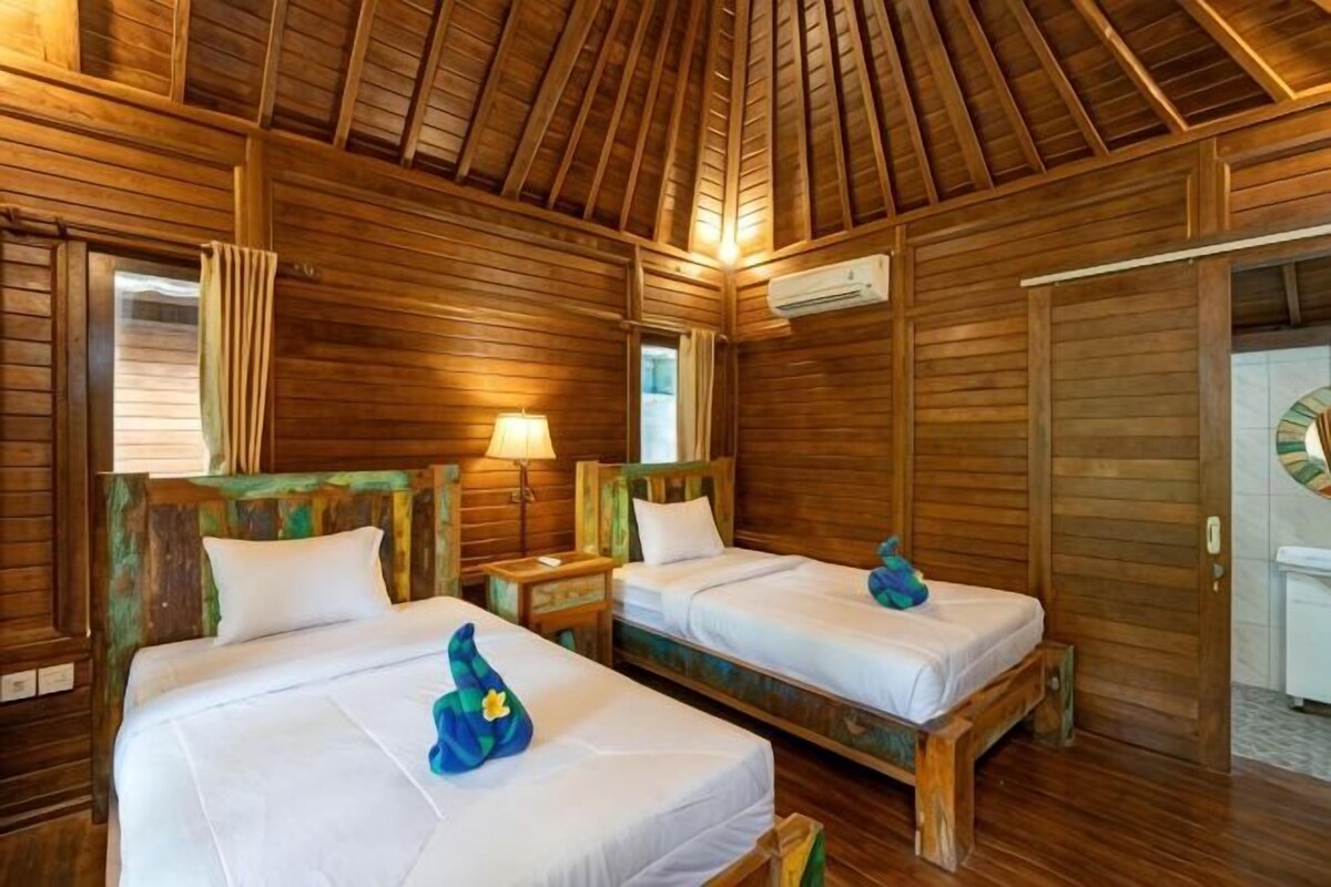 Ein holzgetäfeltes Zimmer im Blockhausstil mit zwei Betten, einem Nachttisch, einer Lampe und einer Tür mit einer Uhr.