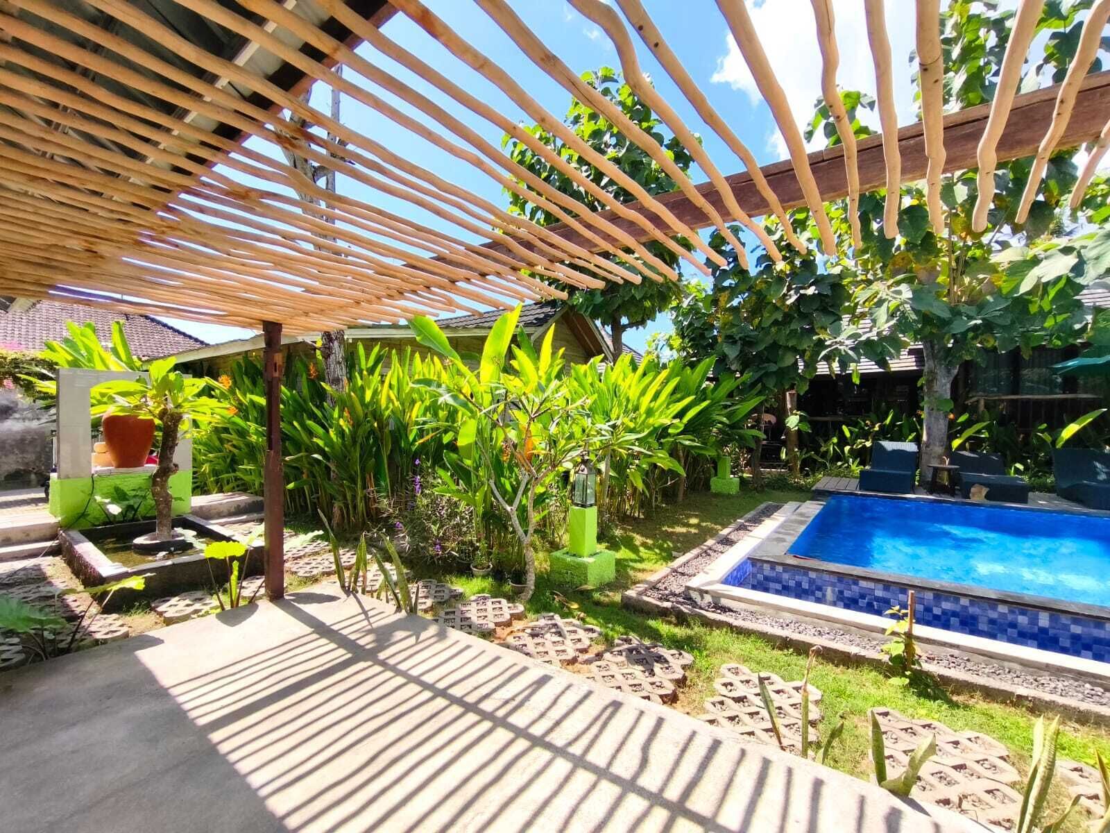 Un área de piscina con una pérgola de madera, rodeada de exuberante vegetación y un pequeño jardín.