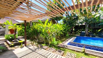 Un área de piscina con una pérgola de madera, rodeada de exuberante vegetación y un pequeño jardín.
