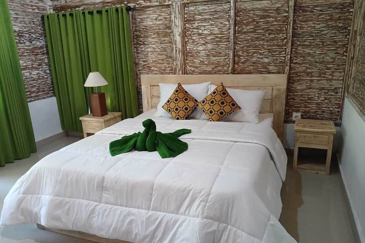 A neatly made bed with a green towel, two patterned pillows, a bedside lamp, and a wooden nightstand.