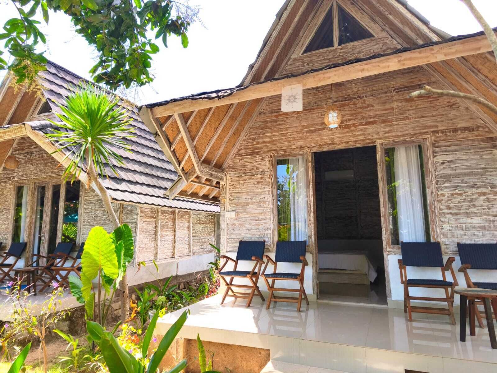 A wooden building with a balcony, outdoor seating, and a tropical garden.