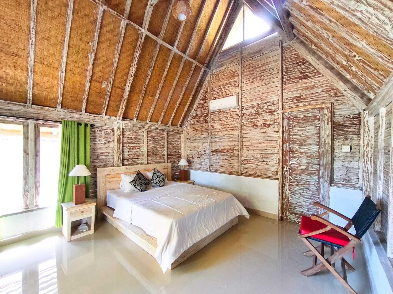 A rustic room with a sloped ceiling, a bed with pillows, a chair, and a window with curtains.